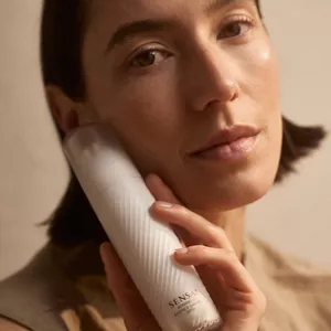 Close up of model holding Advanced Essence Day Veil bottle next to their face 
